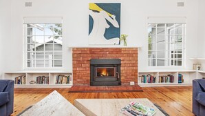 A living room with a brick fireplace, white walls, and bookshelves filled with books.