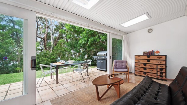 A spacious living area with a sliding glass door leading to a patio, a black leather sofa, a small round table, a purple chair, and a wooden chest of drawers.