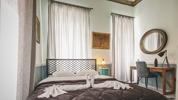 Una cama bien hecha con una colcha oscura de estampado y una toalla doblada en forma de corazón.
