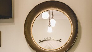 Una habitación con un espejo redondo en la pared, una silla amarilla, una mesa de madera y una escultura blanca.