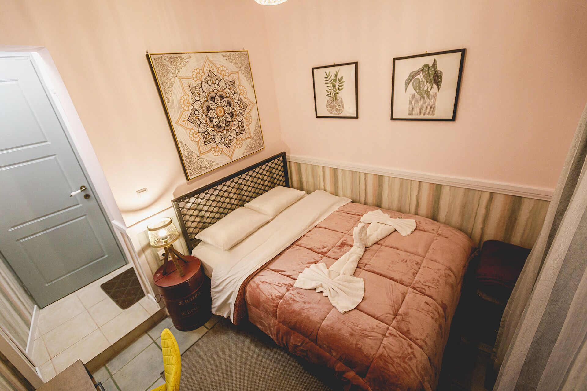 A hotel room with a bed, a nightstand, a lamp, and two framed pictures on the wall.