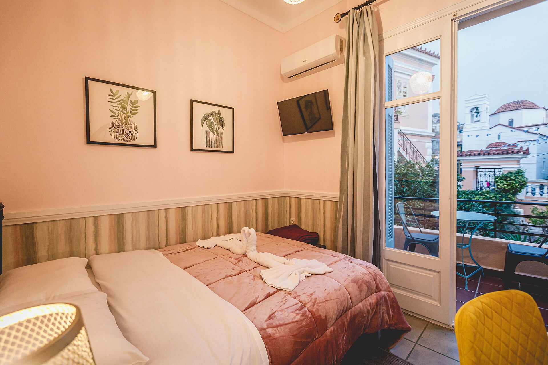 Une chambre d’hôtel avec un lit, une télévision et un balcon donnant sur des immeubles.