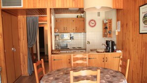 Cucina compatta con mobili in legno, microonde, bollitore e tavolo con sedie.