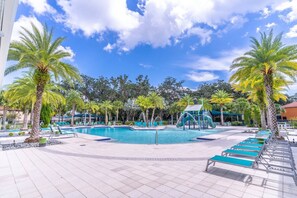 Un espace piscine équipé d’un toboggan, de chaises longues et de palmiers.