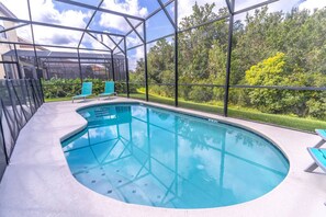 Une piscine dotée d’une enceinte en verre, entourée de verdure et surplombée par un ciel dégagé.