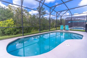Une piscine intérieure aux parois en verre transparent, entourée de verdure et offrant une vue sur le ciel.