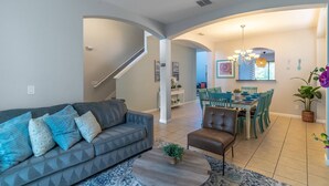 A modern living room with a sofa, coffee table, and dining area with chairs and a chandelier. - 2614 Veranda Palms (Kissimmee)