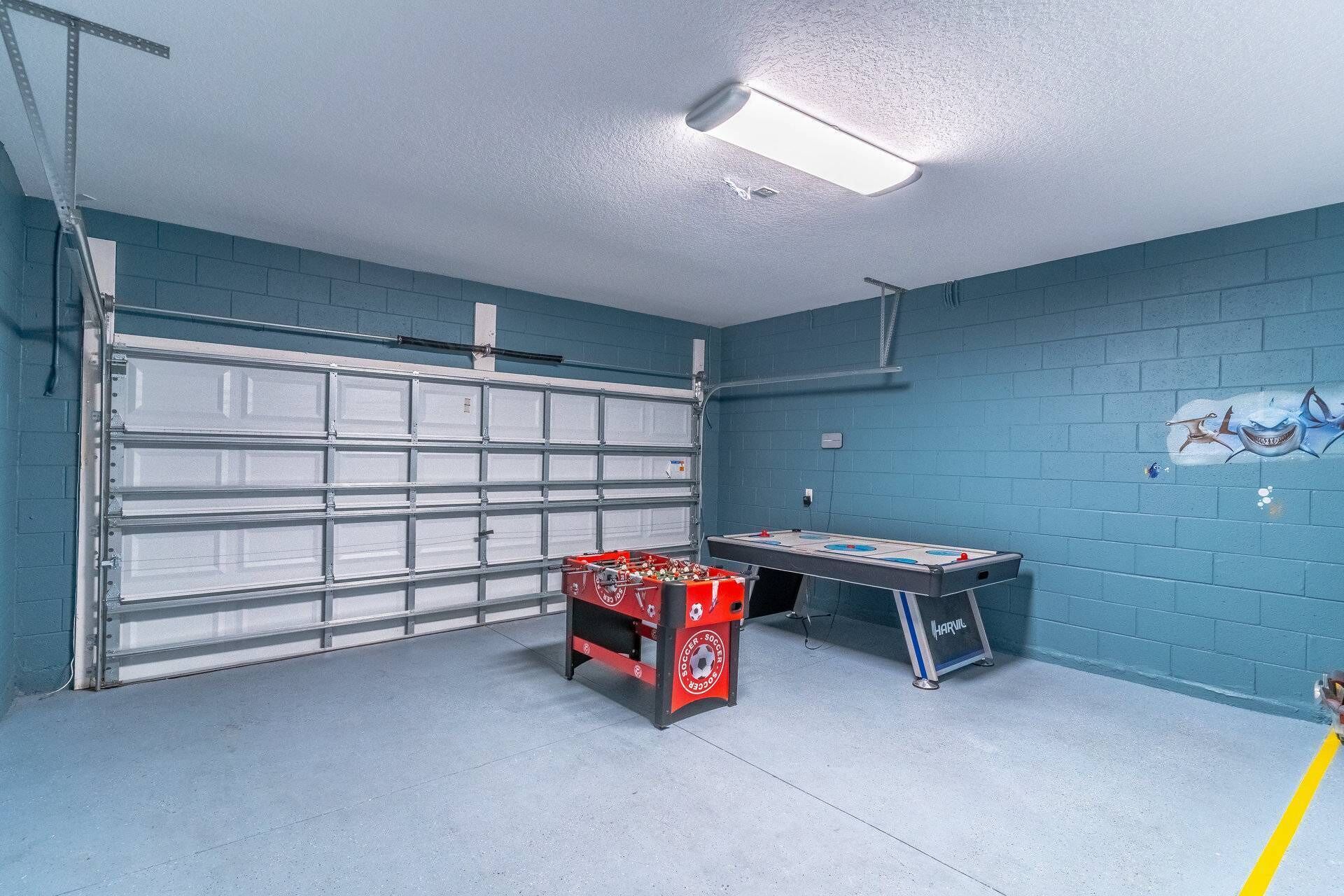Un garage con una parete blu, un portone chiuso, un tavolo da calcio rosso e nero e un tavolo da ping pong.
