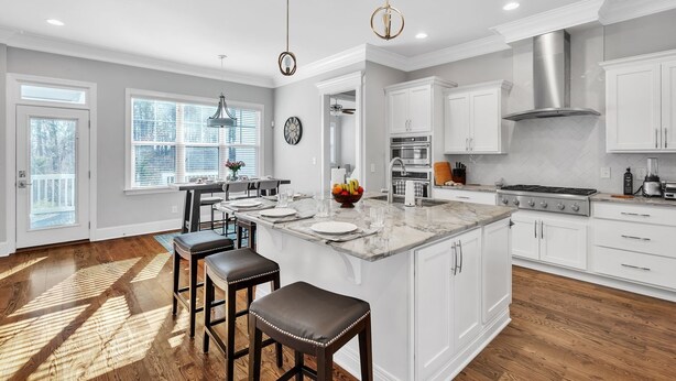A spacious kitchen with white cabinetry, a large island, and a wooden floor. - Durham Retreat Games, Exercise, And Relaxation 5 Bedroom Home (Durham)