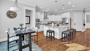 A modern kitchen with white cabinetry, a central island, and a dining area with a black table and white chairs. - Durham Retreat Games, Exercise, And Relaxation 5 Bedroom Home (Durham)