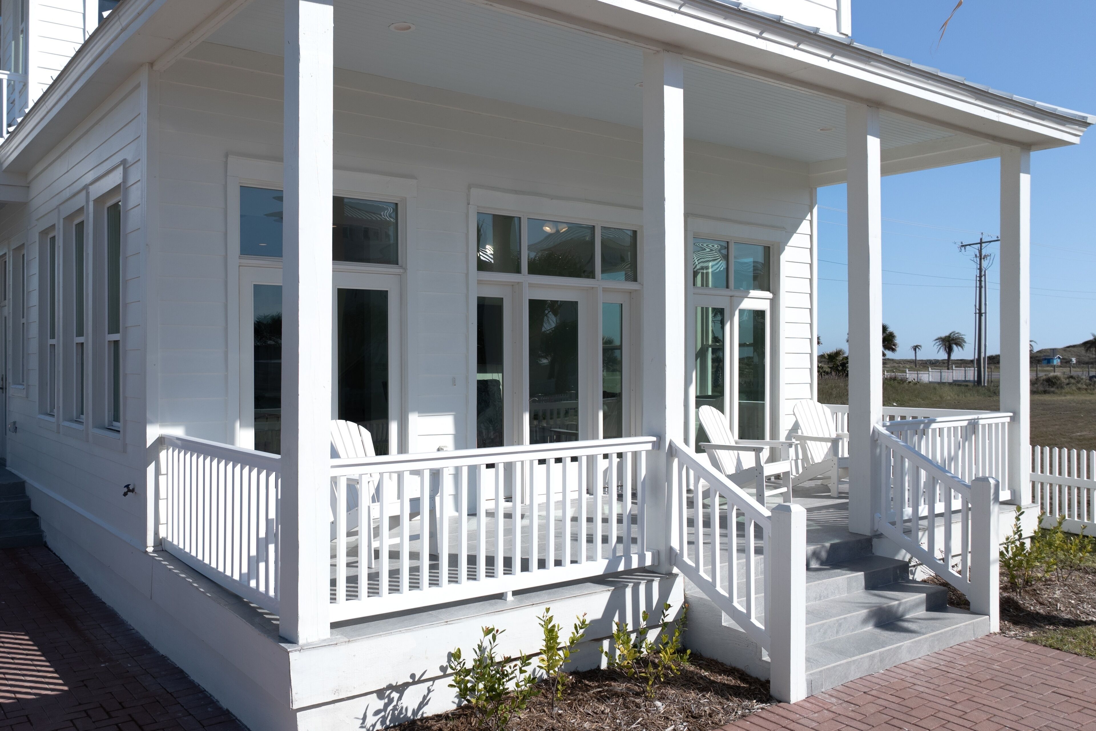 A white house with a covered porch, large windows, and a brick pathway.