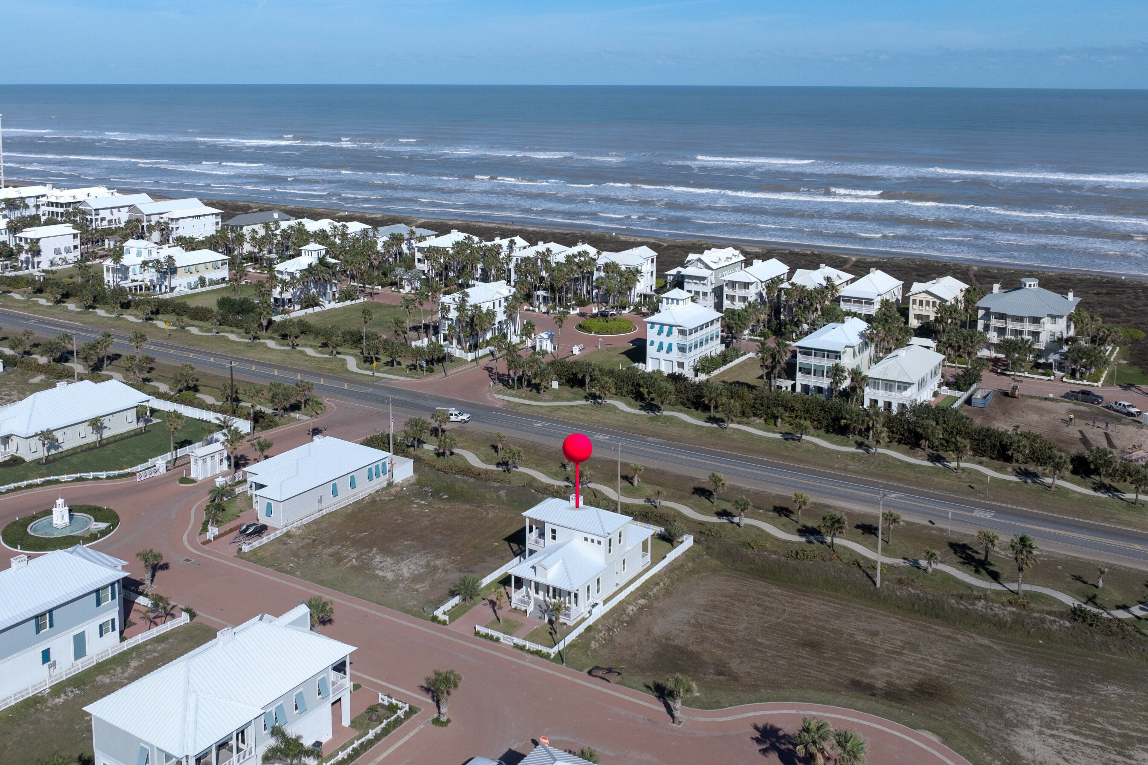 A coastal residential area with white houses, a road, and a beach in the background.