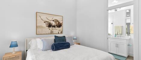 Ein Schlafzimmer mit Bett, Nachttischen, Spiegel und einem Badezimmer mit Waschbecken und Spiegel.