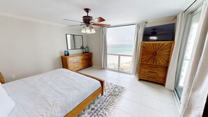 A bedroom with a bed, a dresser, a vanity, a ceiling fan, and a large window with a view of the beach. - Shoreline Towers 1074 2 Bedroom Condo (Destin)