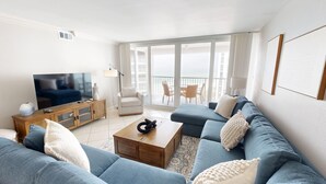 A modern living room with a large TV, a wooden coffee table, and a blue sofa. - Shoreline Towers 1074 2 Bedroom Condo (Destin)