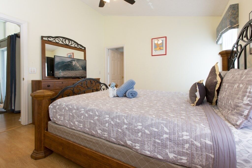 A bedroom with a wooden bed, a television on a wooden dresser, and a painting on the wall.
