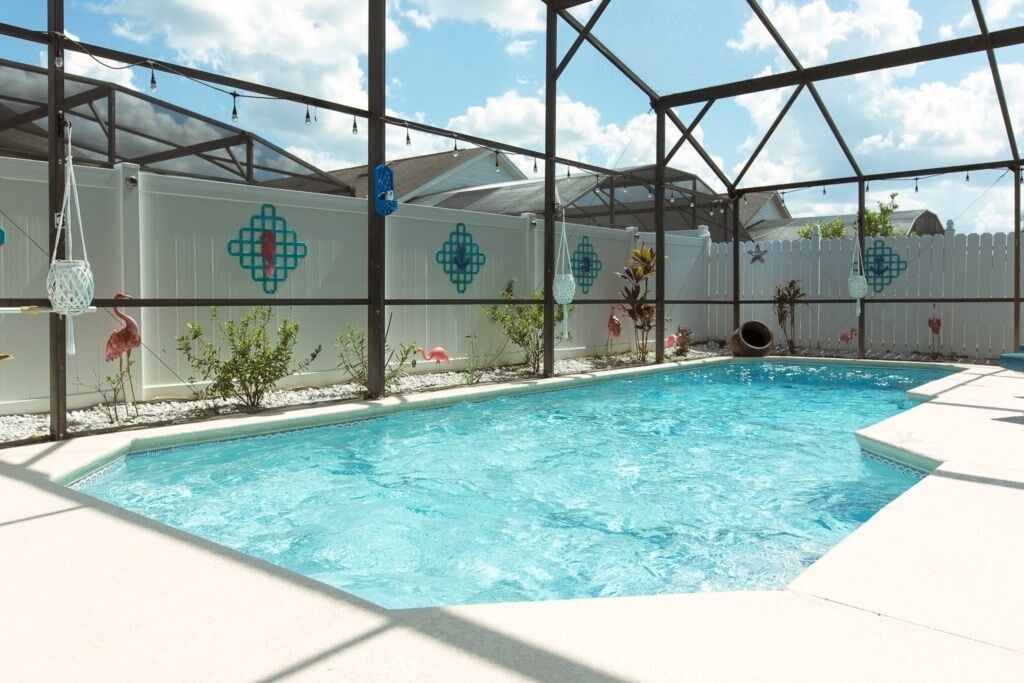 A swimming pool with a white fence, decorative lights, and small plants.