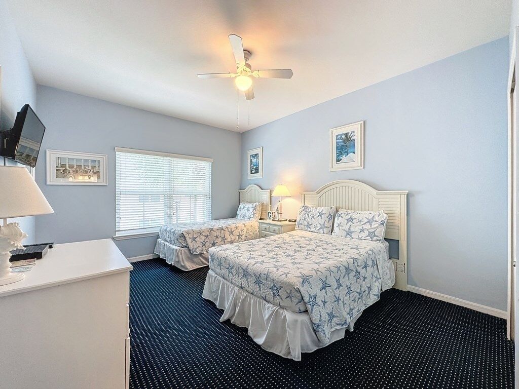 A bedroom with two beds, a desk, and a ceiling fan.