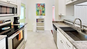 Una cocina moderna con armarios blancos, microondas, estufa y pileta. Hay un cuadro llamativo en la pared y una ventana con vistas.