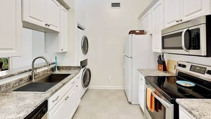 Una cocina compacta con armarios blancos, lavadora y secadora integradas, microondas, horno y un fregadero con encimera de granito.