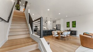 Une cuisine moderne avec un coin repas, un escalier en bois et un salon doté d’un canapé.