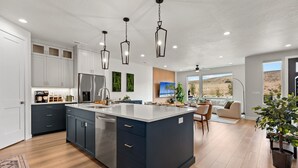Une cuisine moderne dotée d’un îlot central, d’appareils électroménagers intégrés et de luminaires suspendus.