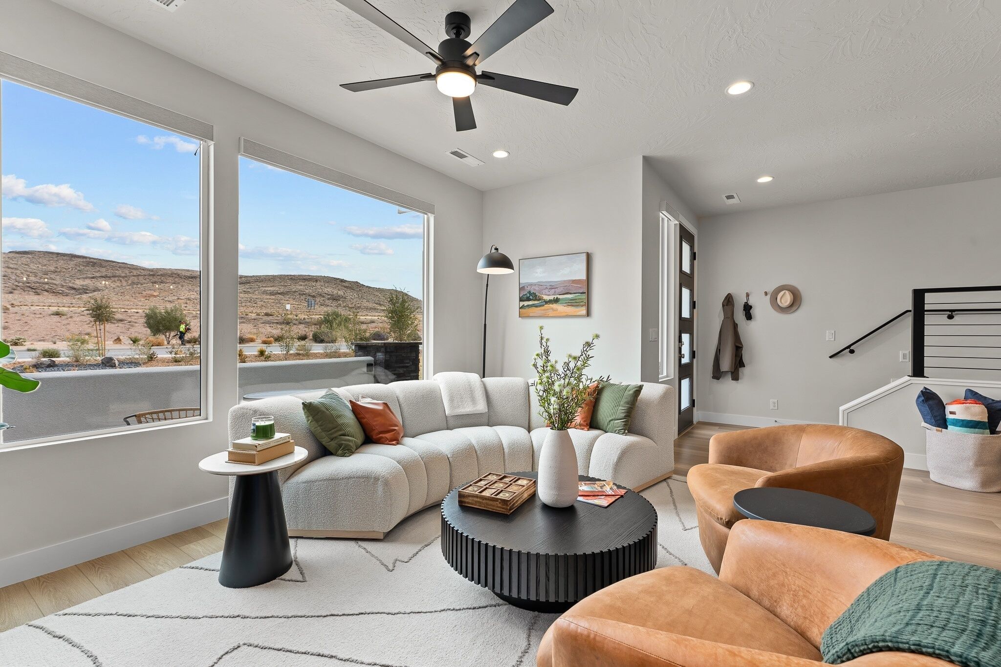 Un salon moderne doté d’une grande fenêtre, d’un ventilateur de plafond, d’un canapé, d’une table basse et d’un fauteuil.