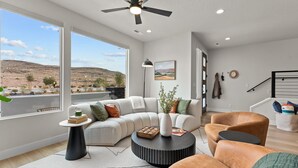 Un salon moderne doté d’une grande fenêtre, d’un ventilateur de plafond, d’un canapé, d’une table basse et d’un fauteuil.