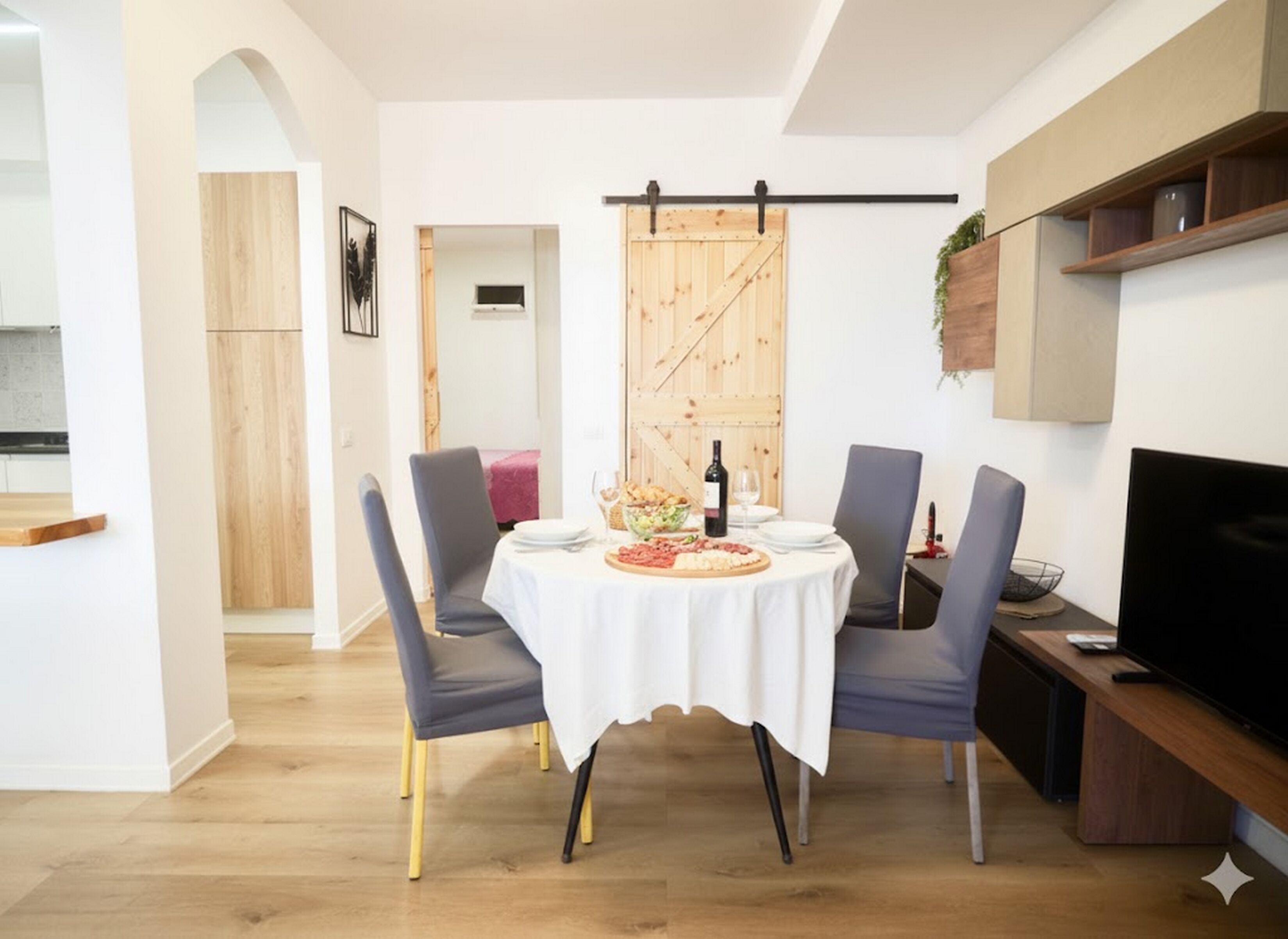 A dining area with a round table, two chairs, a television, and a kitchen in the background.