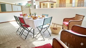 Ein Essbereich mit einem für das Frühstück gedecktem Tisch, umgeben von Korbstühlen und einem Balkon mit Blick auf ein Gebäude.