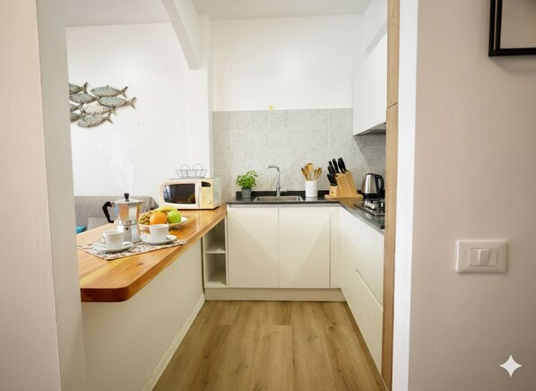 Une cuisine compacte avec des meubles blancs, un plan de travail en bois, un four à micro-ondes, un évier et une machine à café.