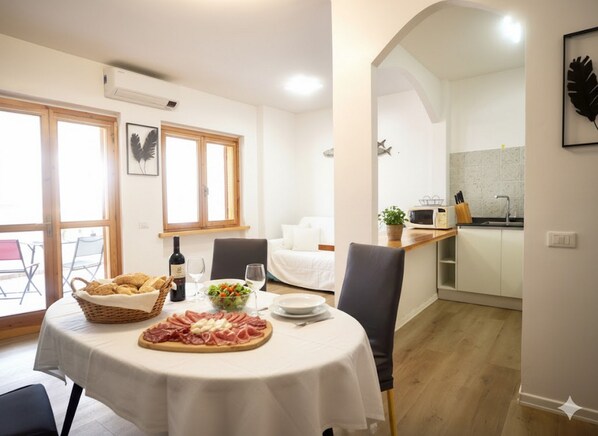 A dining area with a table set for two, featuring a basket of bread, a bottle of wine, and a plate of cured meats. - Appartamento Arcobaleno (Costarainera)