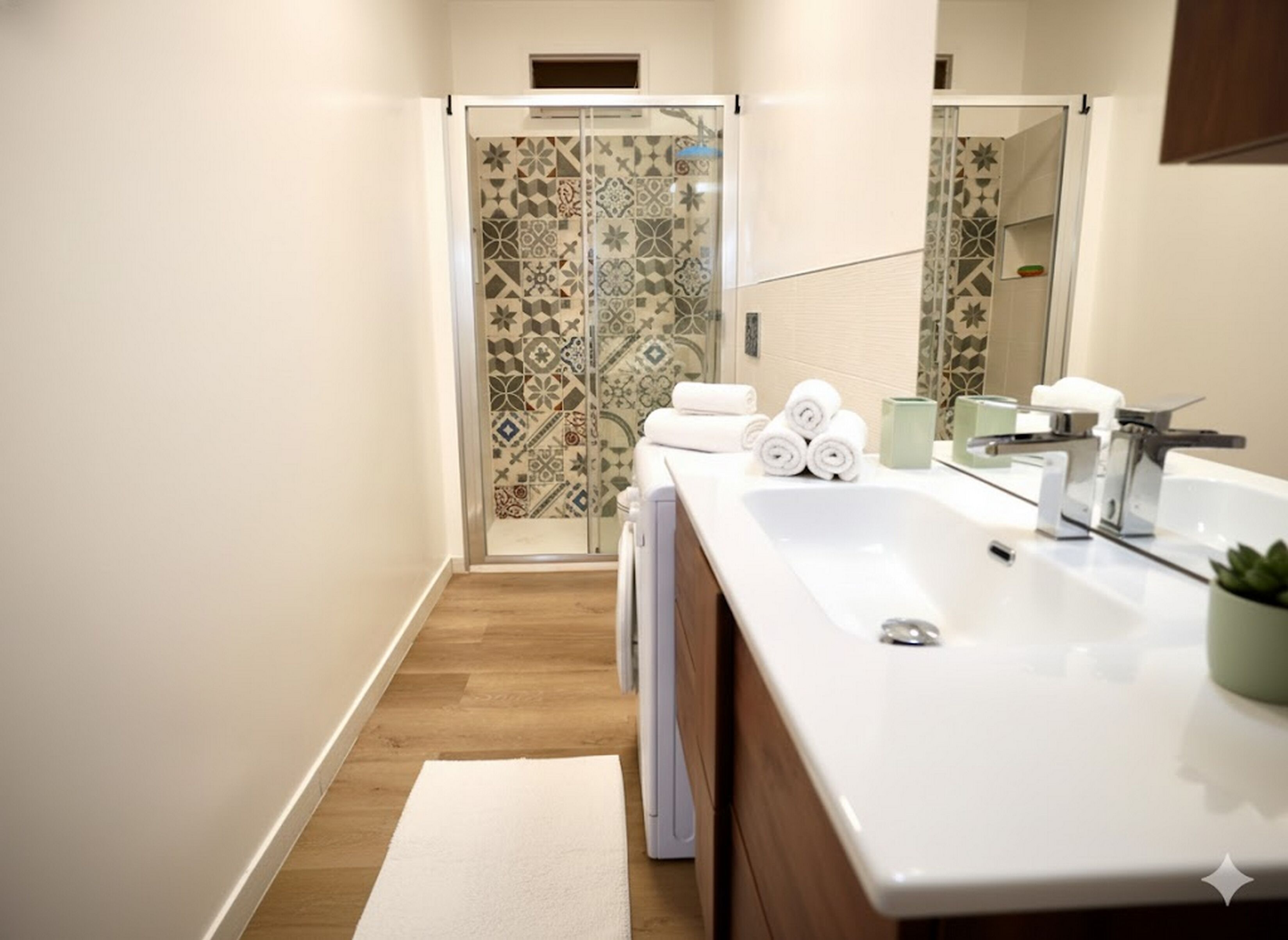 Une salle de bain moderne avec un grand miroir, un lavabo blanc et une douche aux carreaux décorés.