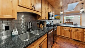 A kitchen with wooden cabinets, granite countertops, stainless steel appliances, and a skylight.