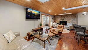 A modern living room with a stone fireplace, wooden ceiling, and a large TV mounted on the wall.