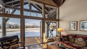 Un salon chaleureux avec une grande fenêtre, un télescope et une vue sur des montagnes enneigées.