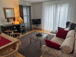 A living room with a sofa, a TV, a cabinet, and a dining area with chairs and a table. - Apartment Sonja - Very cozy (close to the city center!) (Freiburg im Breisgau)