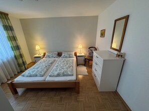 A bedroom with a wooden bed, two bedside tables with lamps, a chair, a dresser, and a mirror on the wall. - Apartment Sonja - Very cozy (close to the city center!) (Freiburg im Breisgau)