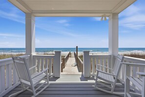 A wooden deck with white railings and benches, leading to a beach with a clear sky.