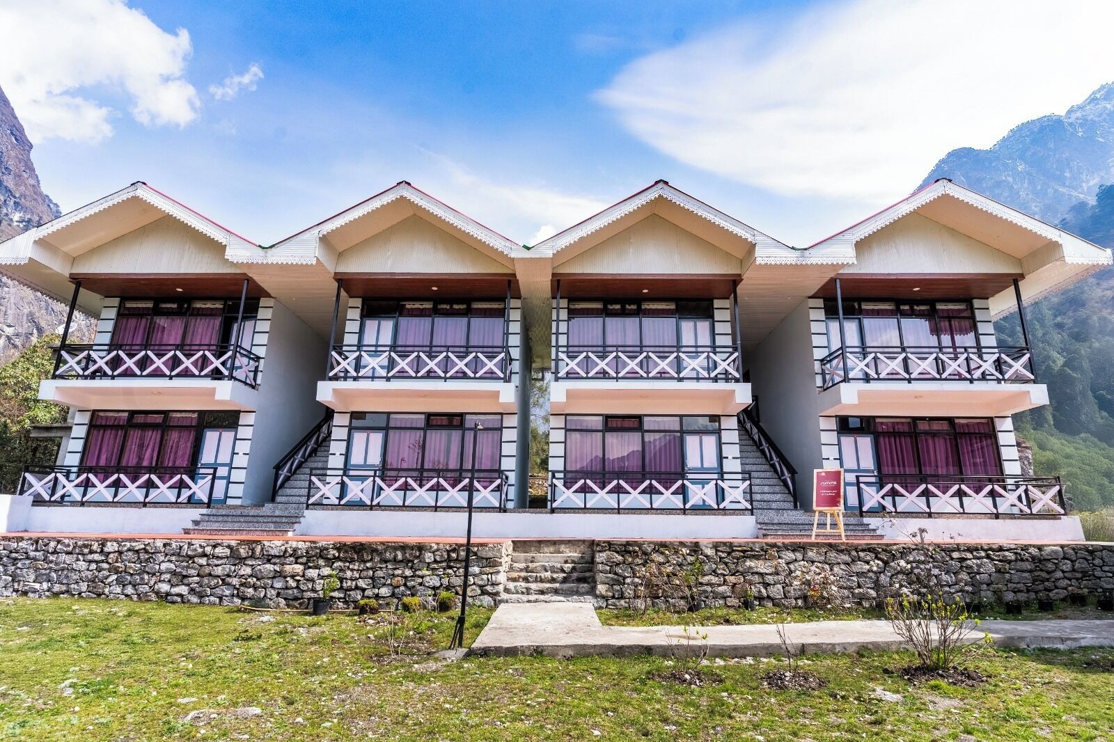 A multi-story building with balconies, stone foundation, and a mountainous backdrop.