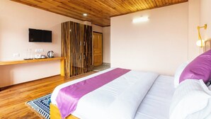 Un dormitorio con techo de madera, una cama con ropa de cama blanca y morada, un televisor en la pared y un armario con espejo.