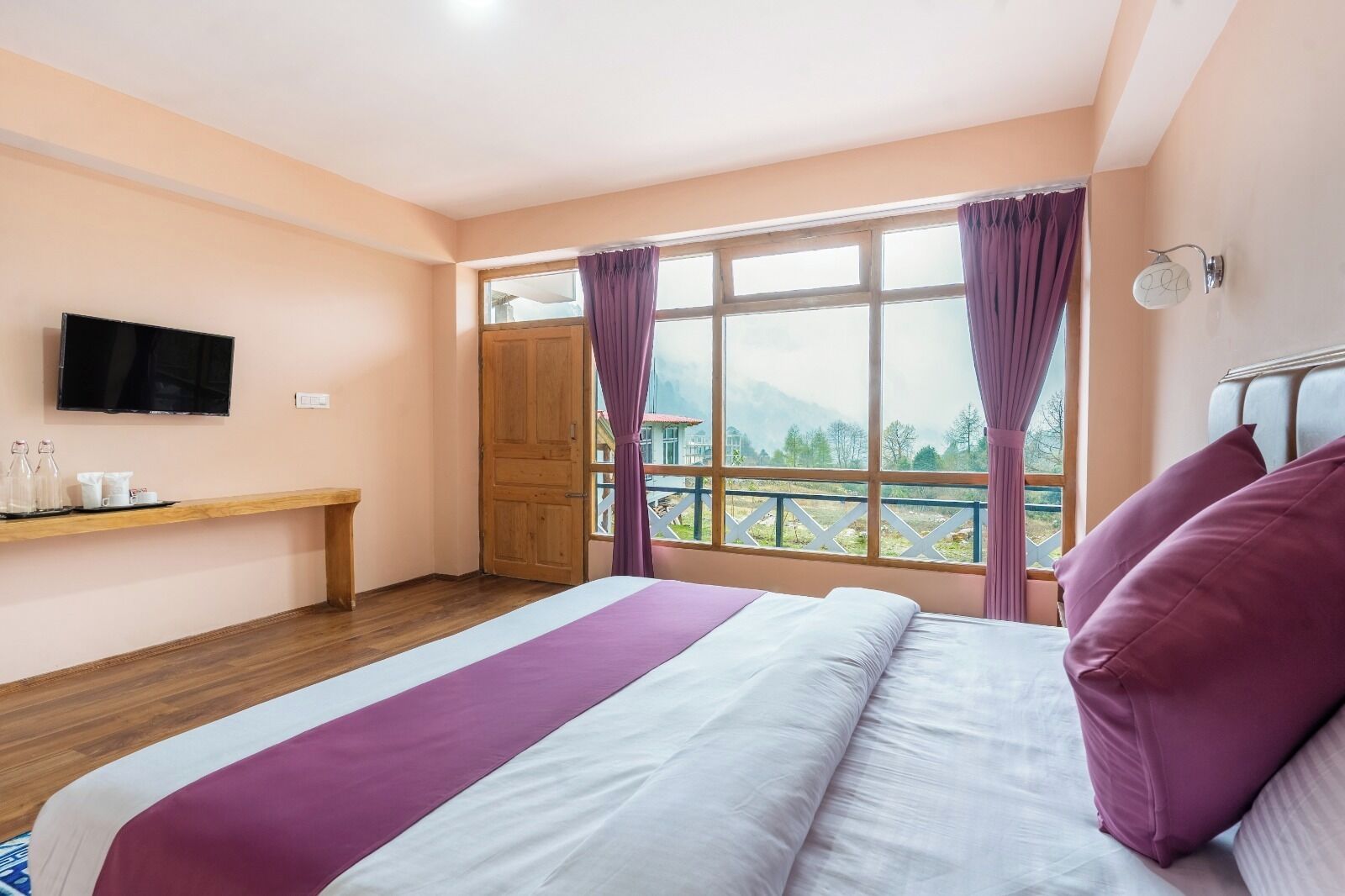 A bedroom with a bed, a TV, a wooden bench, and a balcony with curtains.