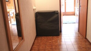 Un couloir avec un sol carrelé, une porte dotée d’un interrupteur et un petit objet noir sur le sol.