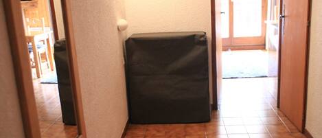 A hallway with a tiled floor, a door with a light switch, and a small black object on the floor.