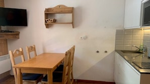 Une petite cuisine avec une table et des chaises en bois, un téléviseur fixé au mur et un pare-feu en carreaux.