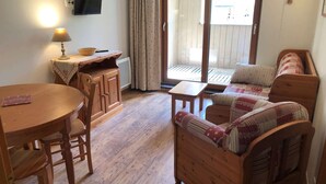 Une pièce chaleureuse avec une table à manger en bois, des chaises, un canapé et un téléviseur fixé au mur.
