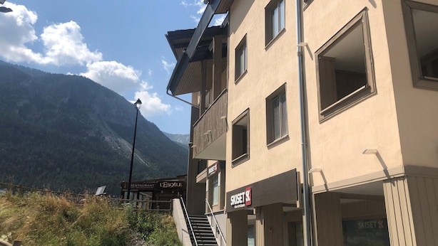 Un immeuble à plusieurs étages qui abrite un restaurant appelé « L’Escale » et une boutique nommée « SKISSET ».