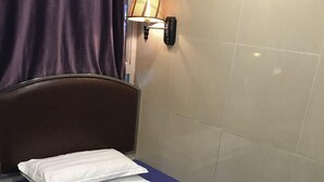 A single bed with a blue mattress, a white pillow, and a wall-mounted lamp. - LIS CHAIN HOSTEL (Kowloon)