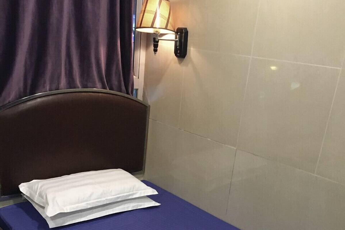 A single bed with a blue mattress, a white pillow, and a wall-mounted lamp.