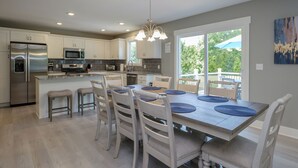 Una cocina moderna con armarios blancos, electrodomésticos de acero inoxidable y un comedor con mesa y sillas de madera.